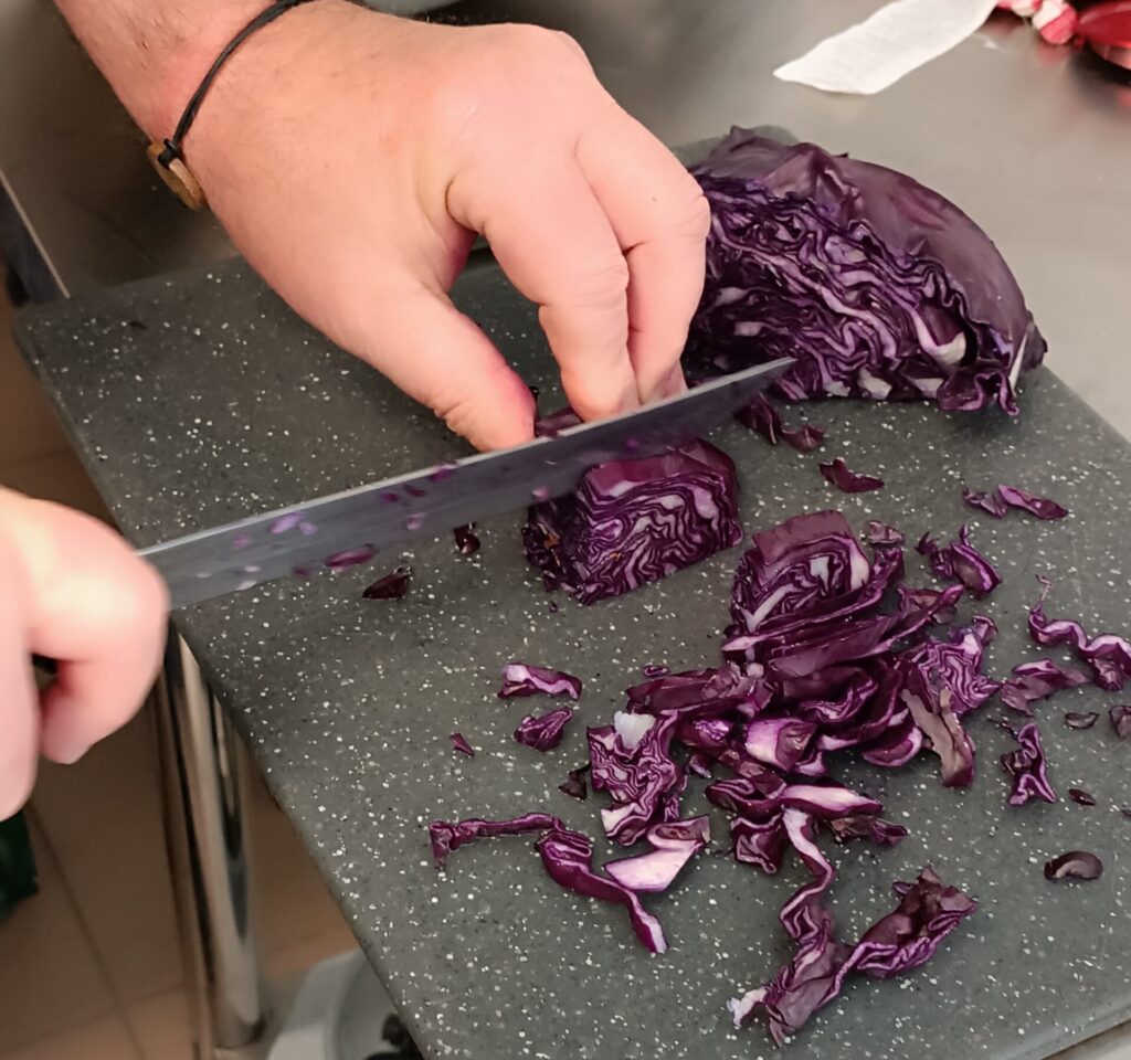 Photo des mains d'un cuisinier de l'entreprise à but d'emploi de Livron-sur-Drôme en train de découper du chou rouge.
