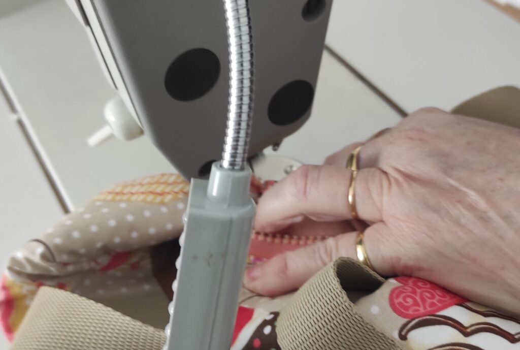 Photo des mains d'une personne en train de coudre à la machine une pochette. La personne est une salariée de l'atelier de couture Les Mains d'Or, à Livron-sur-Drôme.