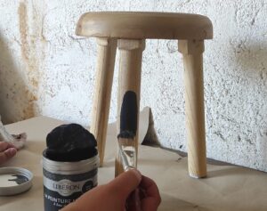 Photo des mains d'une personne en train de peindre un petit tabouret à l'atelier de relooking de meubles de la ressourcerie de Livron-sur-Drôme.